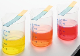 Drei Glasbecher mit farbigen Fluessigkeiten und Teststreifen