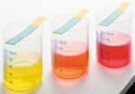 Drei Glasbecher mit farbigen Fluessigkeiten und Teststreifen