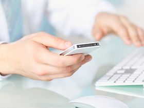 Eine Hand haelt iPhone, andere Hand an Tastatur