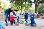 01 Oct 2014, Stockholm, Sweden --- Female teacher assisting girl to ride tricycle on playground ---