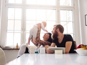Young tattoed mother and father with newborn baby sitting in their kitchen and having fun together