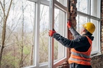 Professional worker in safety gear installs and adjusts large window frames at a new building site