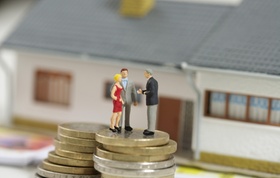 Figuren Paar und Makler auf Stapel aus Euro-Münzen vor Haus