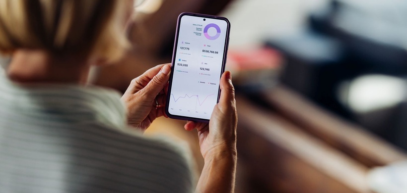 Close-up of a woman using a smartphone to review financial data and analytics at home, focusing on a