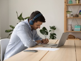 Focused young student guy in earphones watching virtual class, webinar on Internet, online learning