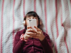 Frau am Handy tippt im Bett