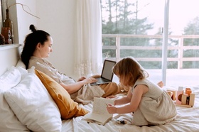 Frau arbeitet am Laptop im Bett während Tochter spielt