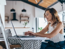 Woman using laptop while sitting at home. Young woman sitting in kitchen and working on laptop