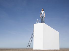 Frau die auf einer Mauer steht an die eine Leiter gelehnt ist