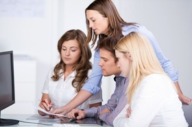 Frau erklärt drei jungen Leuten im Büro etwas am Computer