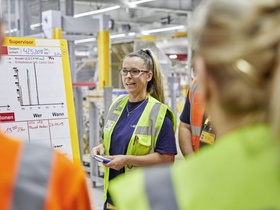 Frau gibt in Fabrikhalle Anweisungen an Team
