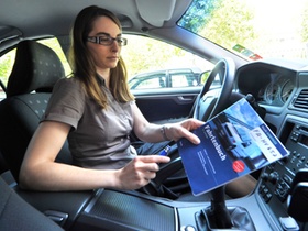 Frau im Auto sitzend hält Fahrtenbuch in der Hand