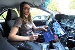 Frau im Auto sitzend hält Fahrtenbuch in der Hand