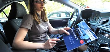 Frau im Auto sitzend hält Fahrtenbuch in der Hand