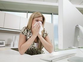 Frau im Büro putzt sich die Nase