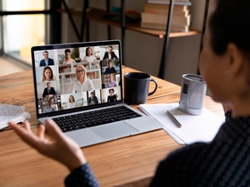 Rear view of female employee talk speak on video call on laptop with diverse colleagues at home offi