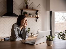 Frau lächelt im Homeoffice am Küchentisch in den Laptop