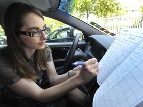 Frau mit Brille sitzt im Auto und schreibt Fahrtenbuch