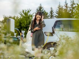 Frau mit Handy beim Laden ihres E-Autos