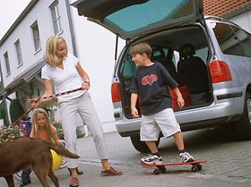 Frau mit Hund an der Leine und Kind auf Skateboard stehen vor geö