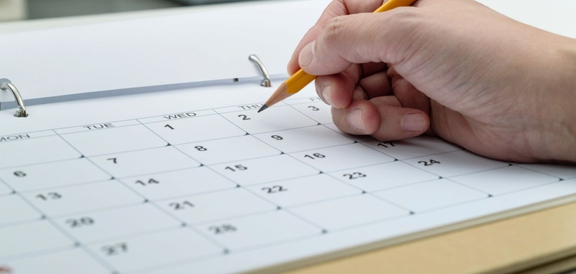 Woman hand with pencil writing on calendar page.
