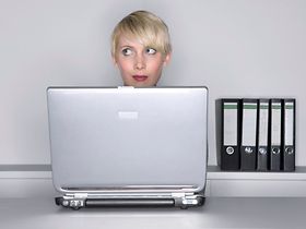 Frau sitzt an Tisch hinter Notebook