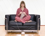 Frau sitzt im Pyjama im Schneidersitz auf Sofa und strickt