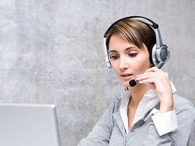 Frau sitzt in Buero mit Headset an Laptop