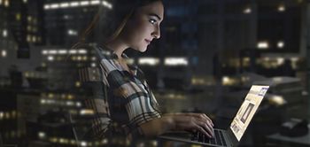 Frau sitzt in der Nacht im Bürogebäude und tippt am Laptop