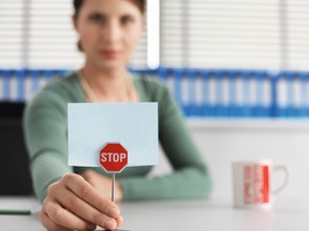 Frau sitzt mit kleinem Stoppschild an Schreibtisch