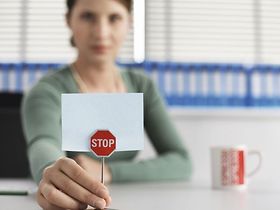 Frau sitzt mit kleinem Stoppschild an Schreibtisch