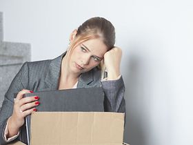 Frau sitzt traurig nach Kündigung mit ihren Sachen auf Treppe