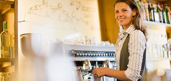 Frau steht hinter der Theke an Profi-Espressomaschine und schaut 