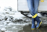 Frau steht mit Gummistiefeln im Schneematsch, Detail Beine