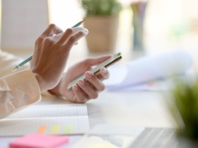 Cropped shot of young businessman using smartphone while working on his project in office room