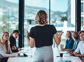 Frau trägt etwas an einem Konferenztisch mit 6 Personen vor