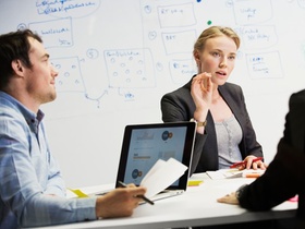 Frau und Männer mit Laptop vor Whiteboard