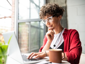 Busy young elegant woman in eyeglasses looking at laptop display while pressing keys of keypad durin