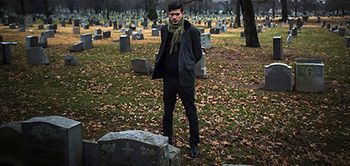 Friedhof mit Mann der auf einen Grabstein blickt