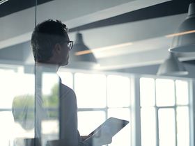 Führungskräft hält hinter Glas ein Tablet in der Hand