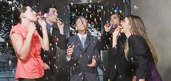 Fünf Kollegen am Konferenztisch mit Tröten und Konfetti