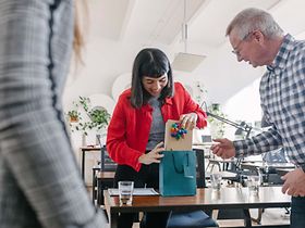 Geschäftliche_Zuwendungen_Frau_öffnet_Geschenk_im_Büro