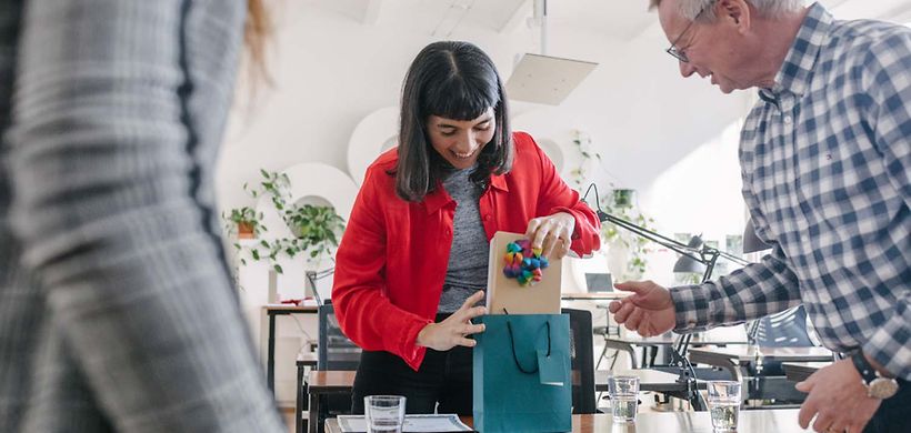 Geschäftliche_Zuwendungen_Frau_öffnet_Geschenk_im_Büro