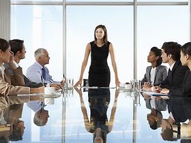 Geschäftsfrau steht an Meetingtisch und spricht in die Runde