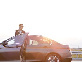 Geschäftsfrau steigt telefonierend aus Dienstwagen