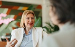 A professional woman converses during a business meeting, with vibrant contemporary decor in the bac