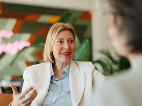 A professional woman converses during a business meeting, with vibrant contemporary decor in the bac
