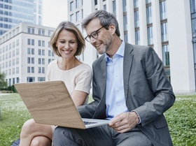Smiling businesswoman and businessman sharing laptop outdoors