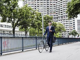 Geschäftsmann läuft mit Fahrrad an Brücke entlang 