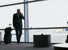 Geschäftsmann mit Gepäck telefoniert am Flughafen